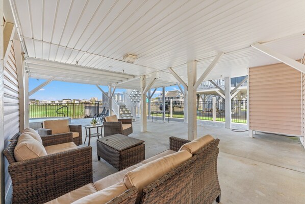 A covered outdoor patio with wicker furniture, a table, and a view of the neighborhood.