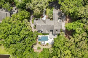 An aerial view of a house with a swimming pool, surrounded by dense greenery.