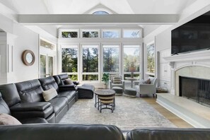 A spacious living room with a fireplace, large windows, and a black leather sofa.