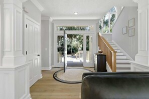 A hallway with a wooden floor, white walls, a black leather sofa, and a staircase with a wooden railing.