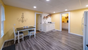Una cucina funzionale con mobili bianchi e un piano di lavoro, una zona pranzo con tavolo e sedie, e un corridoio che porta al bagno.