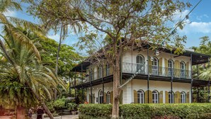 Um edifício de dois andares com varandas, rodeado por vegetação exuberante e palmeiras.