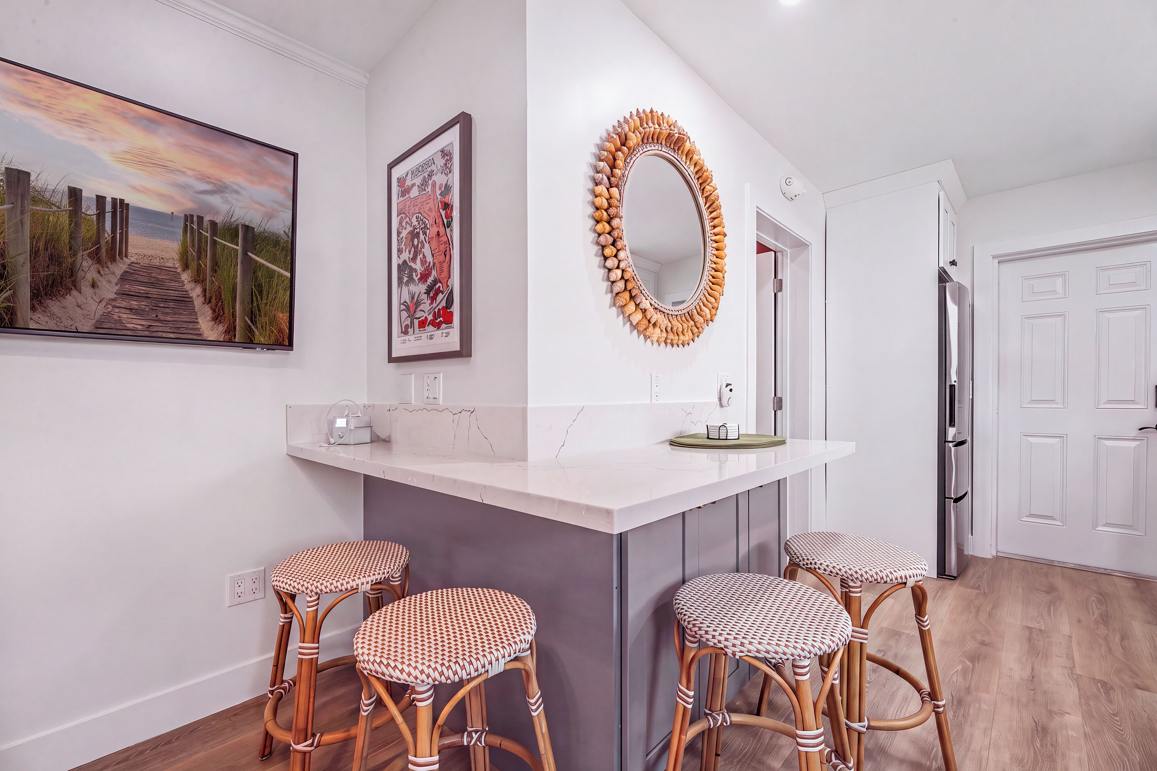 A modern kitchen with a central island, bar stools, a decorative mirror, and a framed picture on the wall.