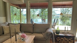 Un salon chaleureux avec un canapé beige, une table basse en bois et une vue sur une terrasse et des arbres, visible à travers de grandes fenêtres.