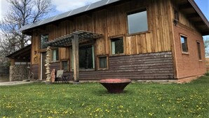 A wooden cabin with a pergola, a stone wall, and a fire pit. - Off-Grid Cottage at Granny Flats (Spearfish)