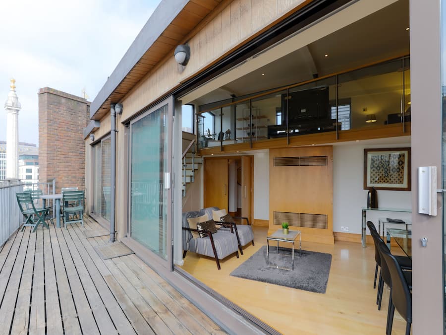 A modern apartment with a balcony, a dining area, and a living room with a sofa and a TV.