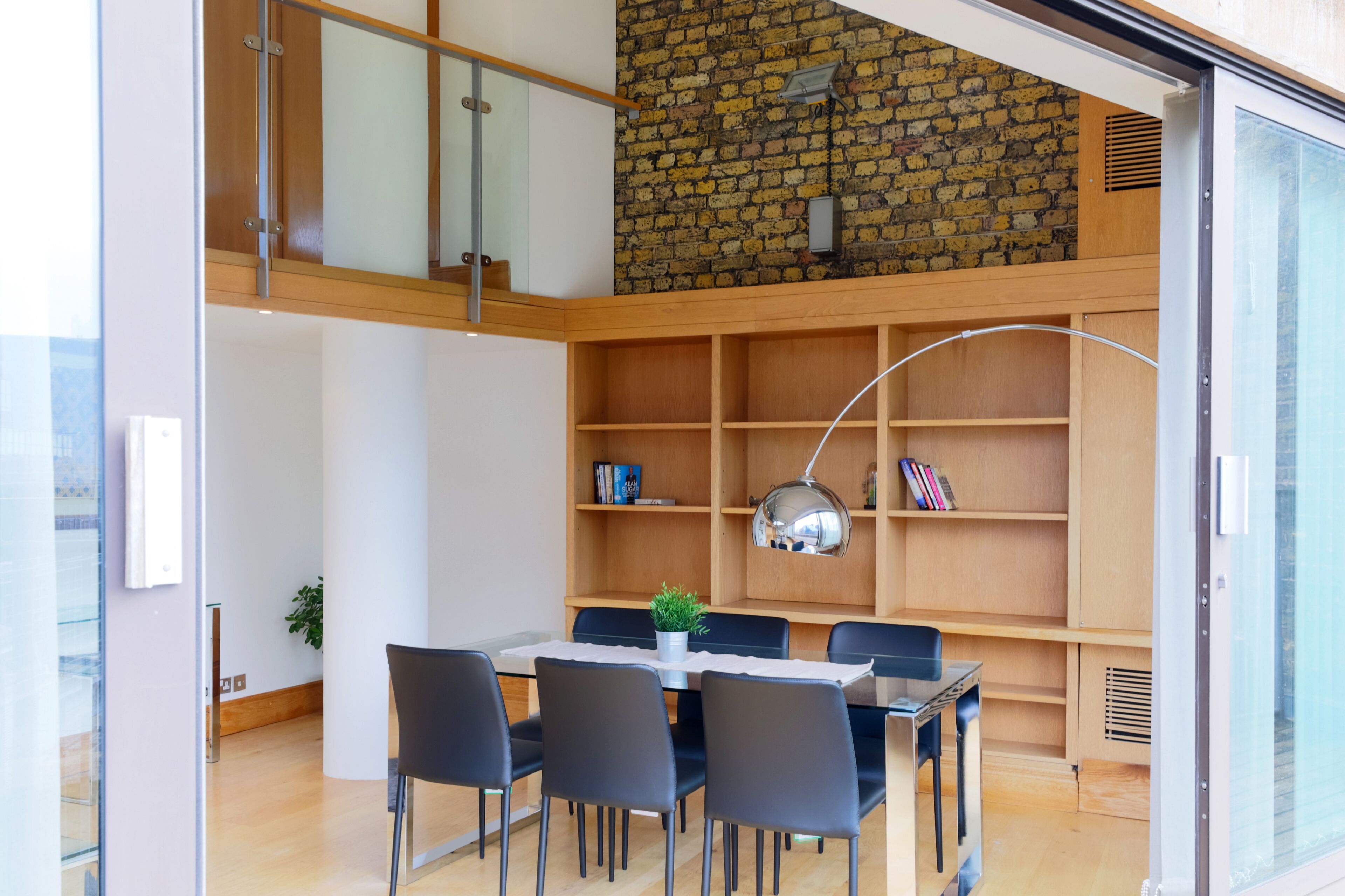 Un espace repas moderne avec une cloison en verre, un mur en briques et une bibliothèque en bois.