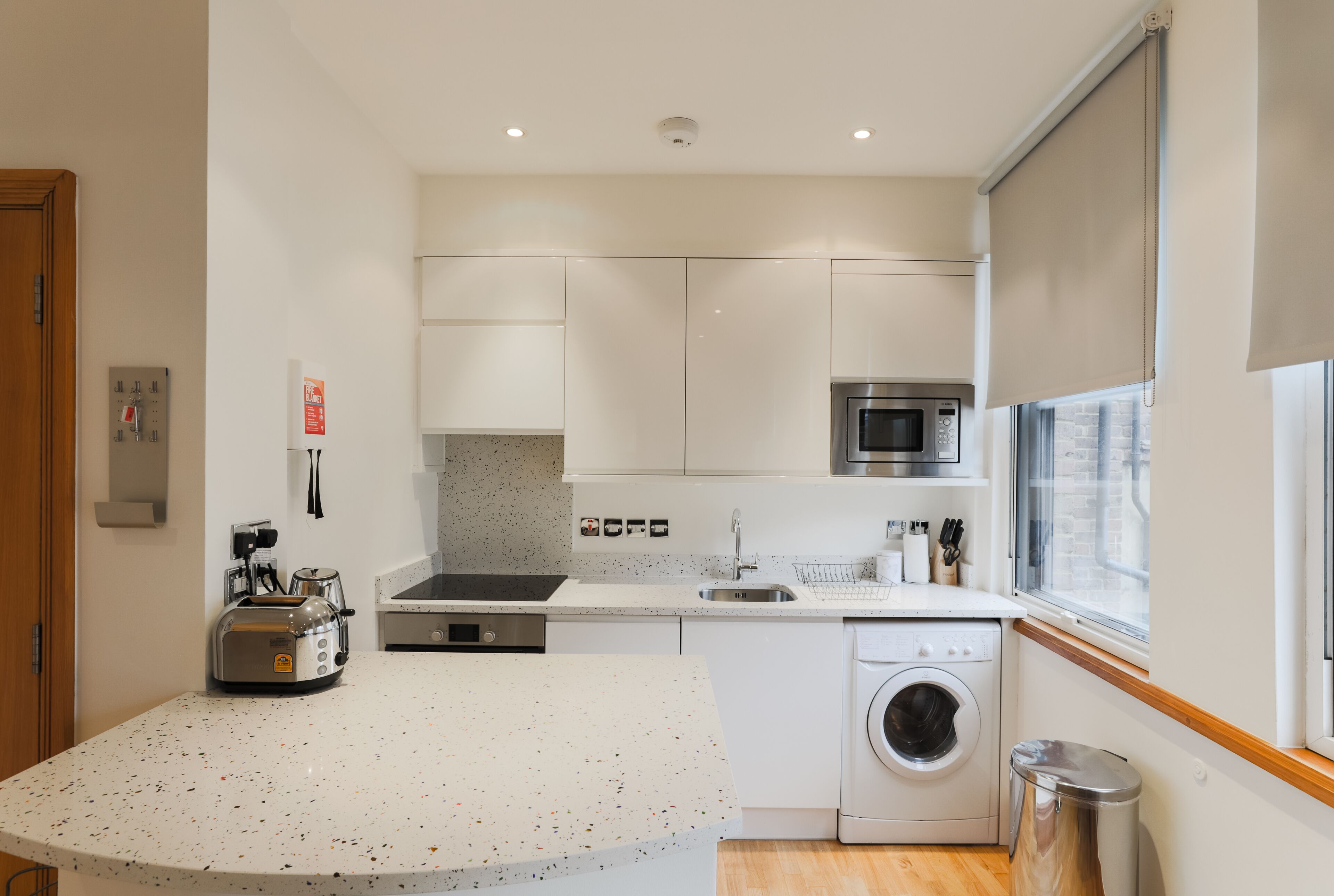 Una cucina moderna con mobili bianchi, un forno a microonde in acciaio inossidabile, una lavatrice integrata e una finestra con vista.