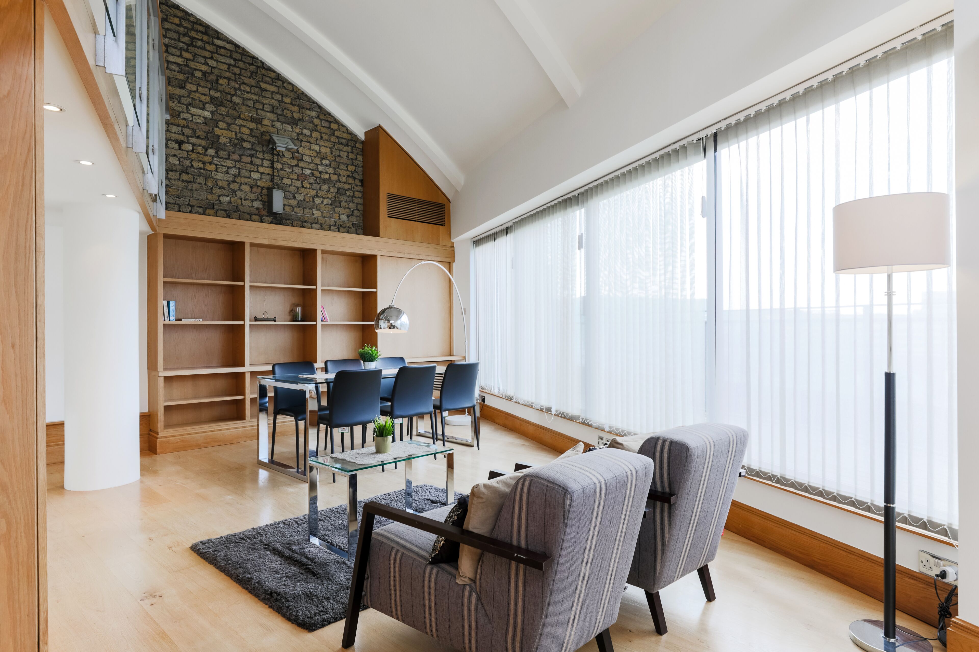 Uma sala de estar moderna com área de jantar, lareira e janelas amplas.