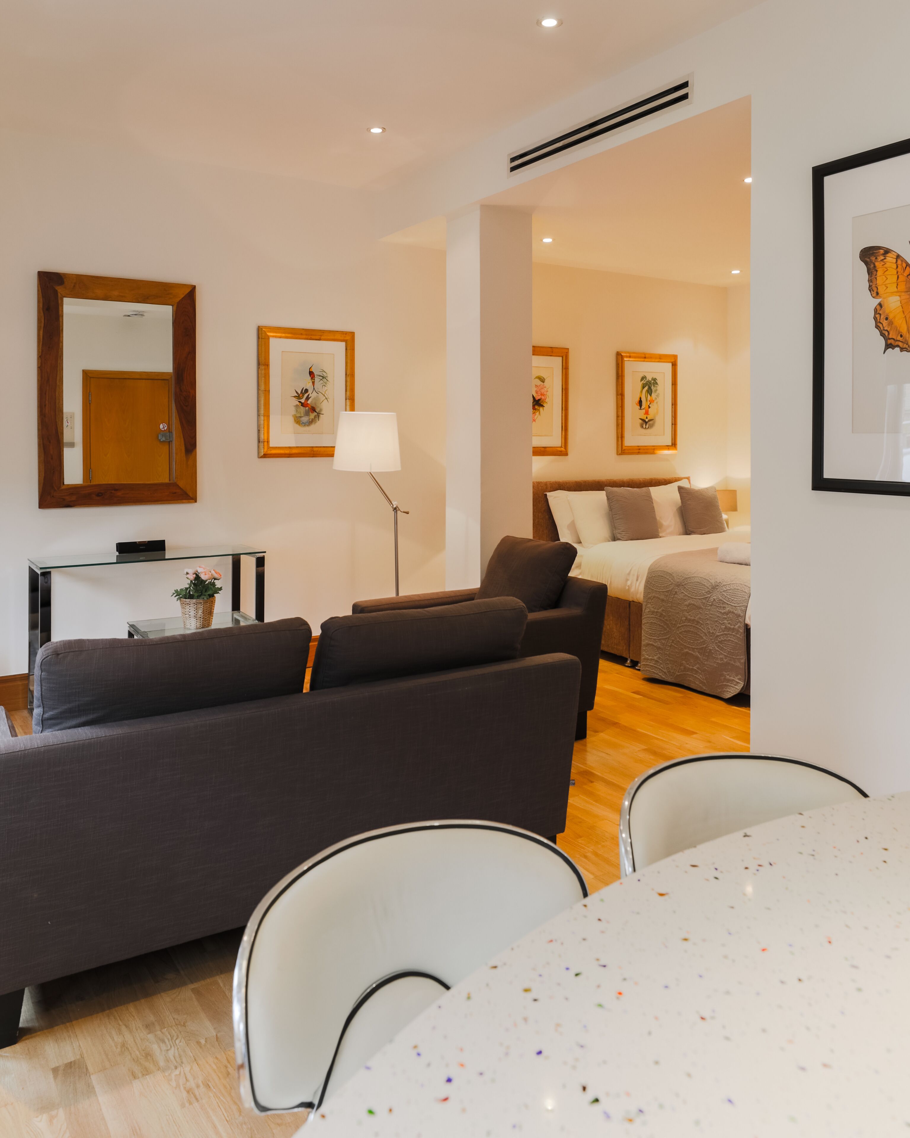 A modern living room with a sofa, a dining table, and a bed in the background.