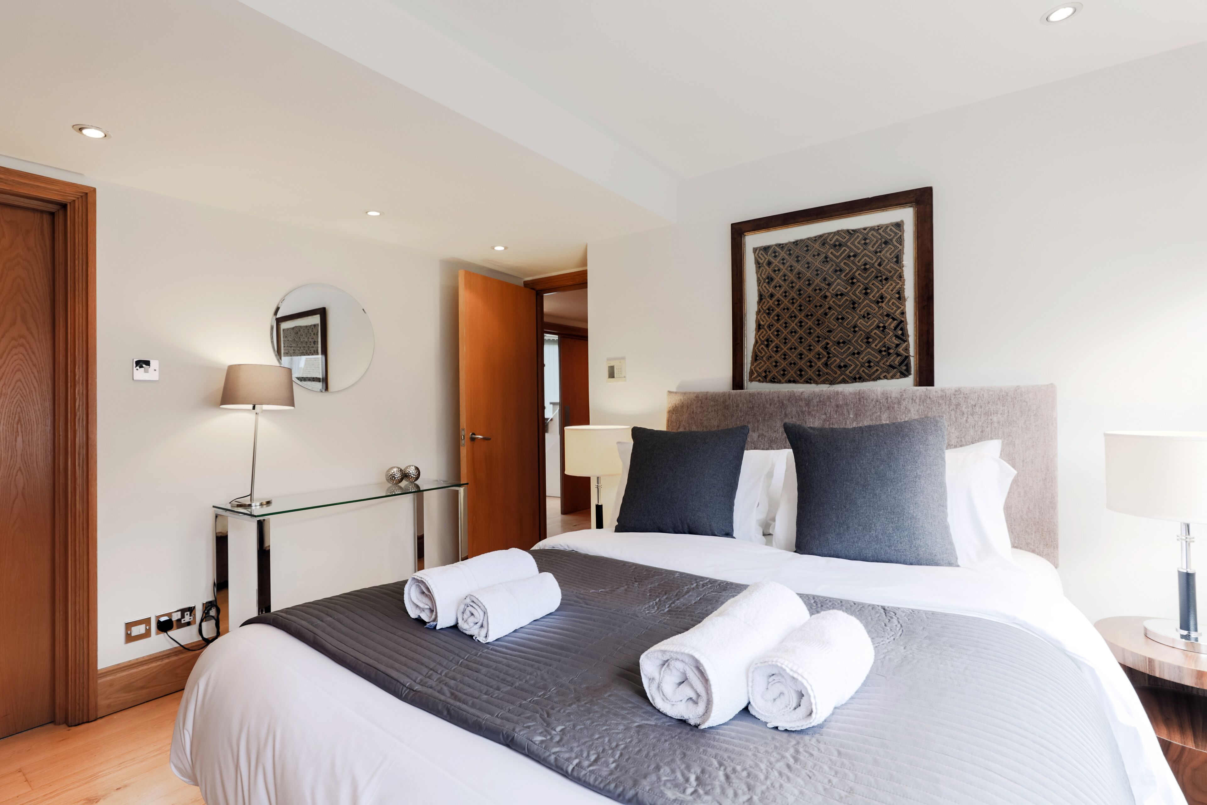 A hotel room with a large bed, a desk with a lamp, and a mirror on the wall.
