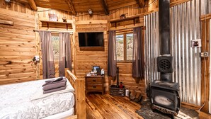 Habitación tipo cabaña de madera con una cama, un escritorio pequeño, un televisor y un estufa de leña.