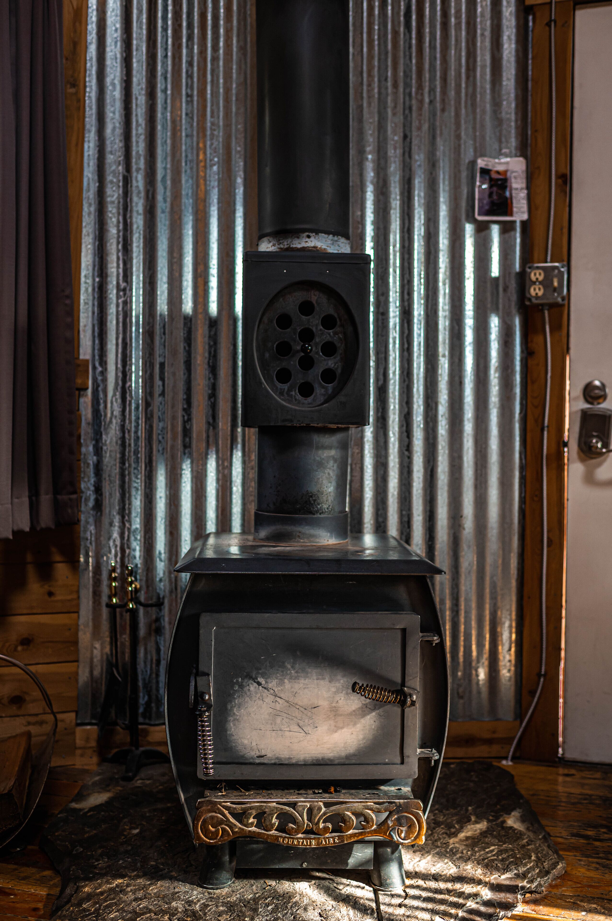 A wood stove in a room with a corrugated metal wall and a wooden door.