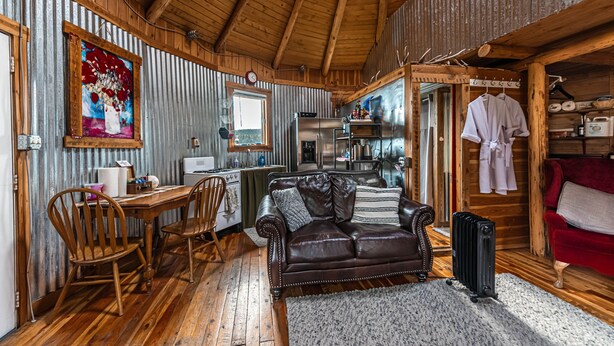 Interior rústico de una cabaña con una mesa de comedor de madera, un sofá de cuero y una zona de cocina.