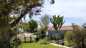 Un espace extérieur verdoyant, avec une clôture en métal, des arbres et un bâtiment avec un toit rouge en arrière-plan.