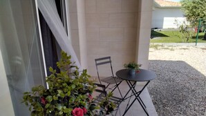 Une terrasse avec une petite table ronde et une chaise, un pot de fleurs et une fenêtre avec un rideau.