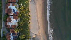 An aerial view of a beachfront property with multiple buildings, a sandy beach, and palm trees. - Deluxe Beachfront Villa (La cruz de Huanacaxtle)