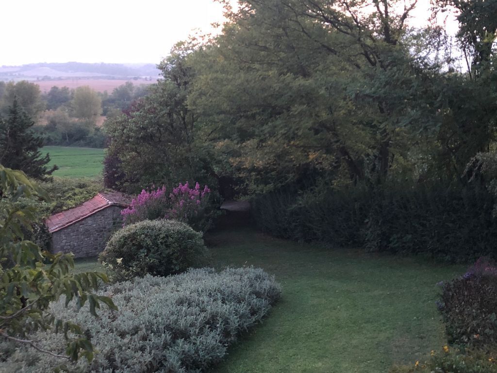 Ein Garten mit einem Steinhaus, verschiedenen Sträuchern und einer Rasenfläche.