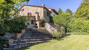 Ein Haus aus Stein mit rotem Ziegeldach, einer Steintreppe, die zum Eingang führt, und einem gepflegten Rasen.
