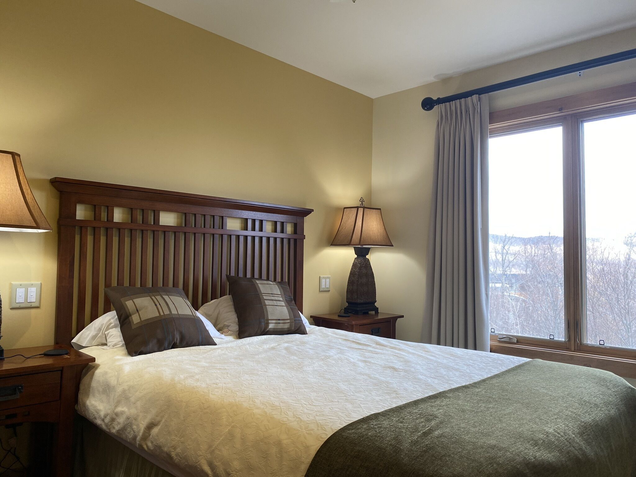 A hotel room with a bed, a nightstand, a lamp, and a window with curtains.