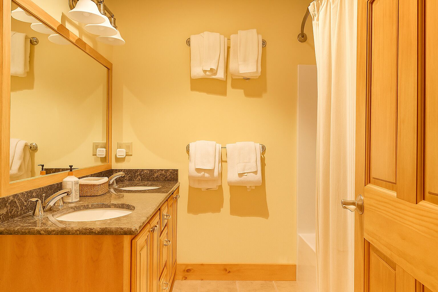 A bathroom with two sinks, a large mirror, and wooden cabinets. There are towels hanging on hooks and a shower curtain visible.