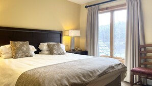 Een hotelkamer met een groot bed, een nachtkastje met een lamp, een stoel en een raam met gordijnen.