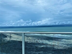 Una spiaggia con ringhiera in vetro, vista sull'oceano e cielo nuvoloso.