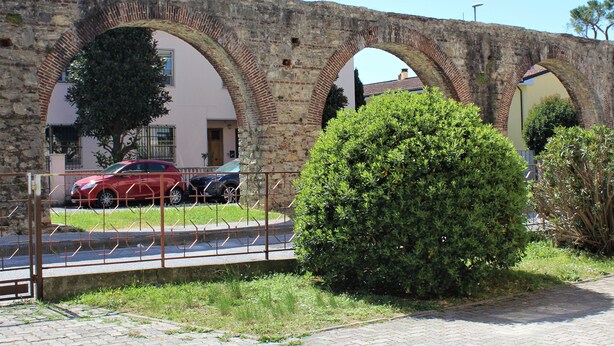 Un arco de piedra con un sendero pavimentado y un seto bien cuidado.