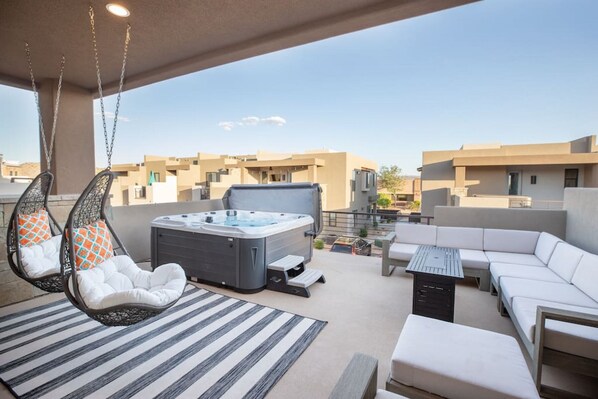 Eine Dachterrasse mit Whirlpool, Hängesesseln und einer Couch.
