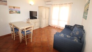 Un salon comprenant un canapé, un téléviseur posé sur un meuble, une table à manger avec des chaises et une fenêtre avec des rideaux.