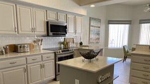 Una cocina moderna con armarios blancos, microondas integrado, tostadora y estación de café.