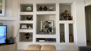 Una sala de estar con pared blanca, estanterías con adornos, un globo terráqueo y un televisor.