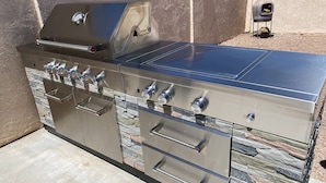 Una cocina exterior de acero inoxidable con múltiples hornillas, una parrilla y un ahumador integrado.