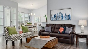 A modern living room with a brown leather sofa, patterned armchairs, a coffee table, and a cityscape painting on the wall. - Water Well Wonder|Near Apple & Domain|Pet Friendly (Austin)
