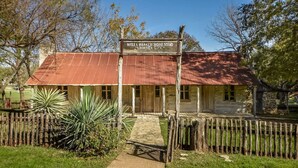 A rustic building labeled "Wells Branch Homestead" with a metal roof, surrounded by a wooden fence and a paved path leading to the entrance. - Water Well Wonder|Near Apple & Domain|Pet Friendly (Austin)