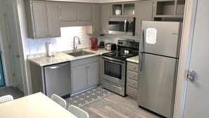 A modern kitchen with grey cabinets, stainless steel appliances, a sink, and a dining area with a table and chairs. - Uncrowded Beachfront Getaway with an Ocean View (Murrells Inlet)