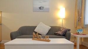 A living room with a grey sofa, a white coffee table, and a small side table with a book and a vase. - Haus Sarah 4 is located directly on the beach in the heart of Westerland.<br>The beach crossing to Westerland's central beach is about 200 meters away.<br>The house has 8 modern and comfortably furnished vacation apartments for. (Westerland)