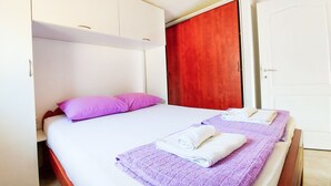 Ein Doppelbett mit zwei Kissen, ein roter Kleiderschrank und zwei Handtücher auf einem violetten Bettüberwurf.