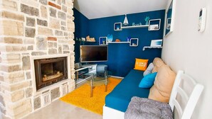 Ein Wohnzimmer mit Kamin aus Stein, einem Flachbildfernseher, einem blauen Sofa mit Kissen und dekorativen Regalen an der Wand.