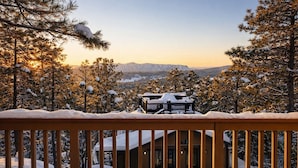 Un paysage enneigé avec une terrasse en bois au premier plan et un bâtiment dont le toit est recouvert de neige en arrière-plan.