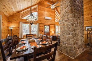 L’intérieur d’un chalet en bois, avec un pilier en pierre, une table à manger dressée pour six personnes et un ventilateur de plafond.