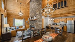 L’intérieur chaleureux d’un chalet avec une cheminée en pierre, un plafond en bois et un coin repas comprenant une table et des chaises.