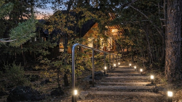 Un escalier en bois mène à un bâtiment entouré d’arbres, et des lampadaires illuminent le chemin.