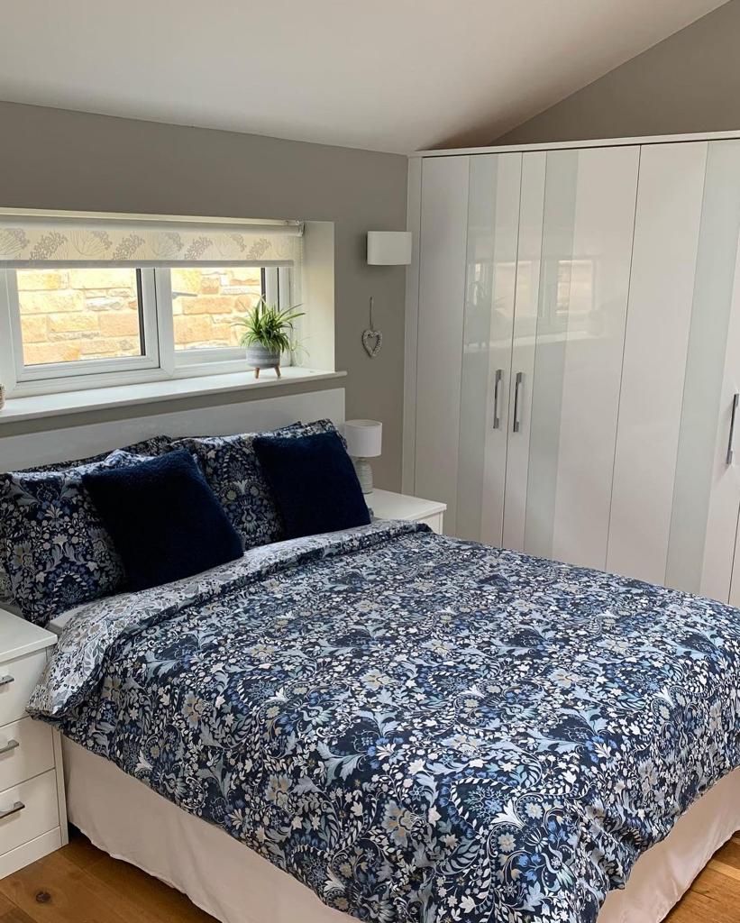 A bedroom with a bed, a window with a plant, a wardrobe, and a bedside table.