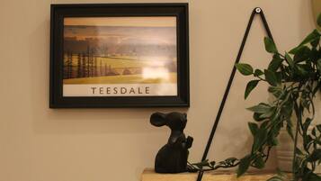 Un tableau encadré représentant Teesdale est accroché au mur, une petite figurine noire est posée sur une étagère, et une plante en pot se trouve à droite.