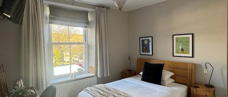A bedroom with a bed, bedside tables, a desk, and a window.