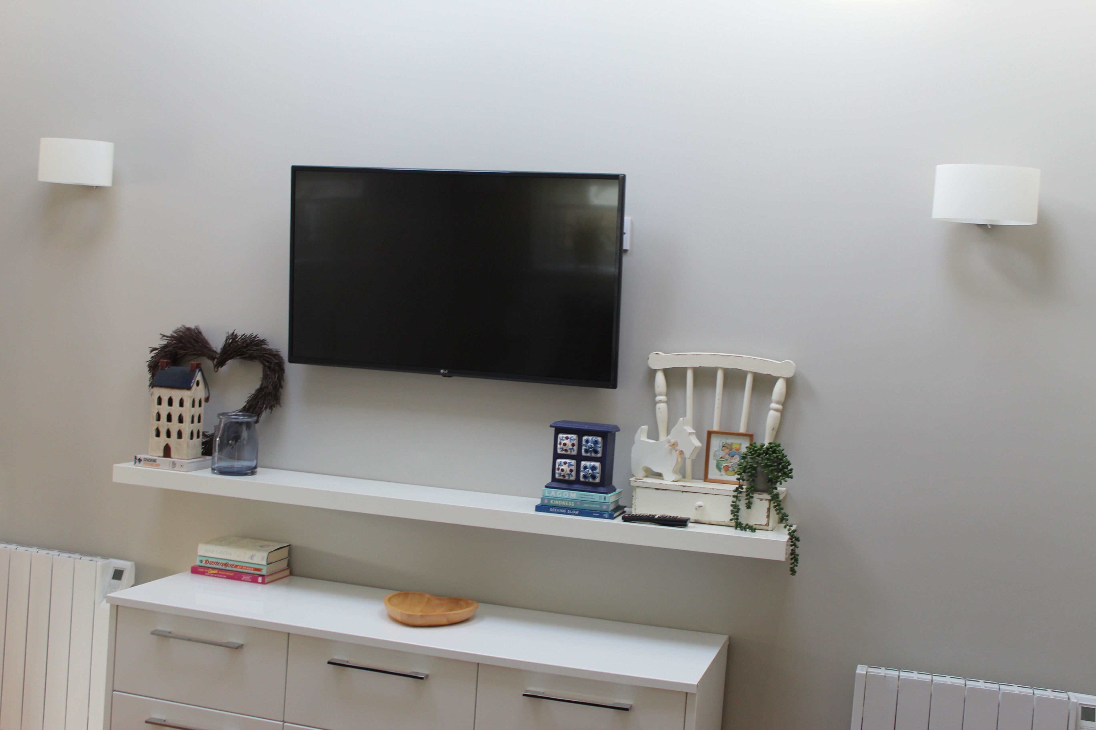 A modern living room with a flat-screen TV mounted on the wall, a white console table with decorative items, and a white radiator below.