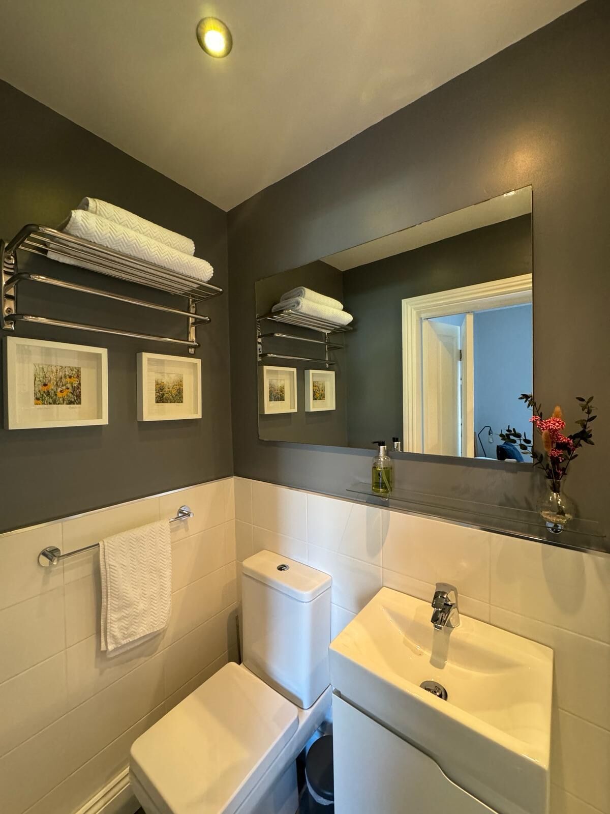 A modern bathroom with a toilet, bidet, and sink, featuring a mirror, towel racks, and framed artwork.