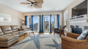 A spacious living room with a leather sofa, a wicker chair, a glass door leading to a balcony, and a fireplace.