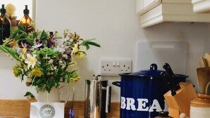 Un plan de travail de cuisine avec une machine à café, un pot bleu portant l’inscription « PAIN », un pot de miel et une planche à découper en bois.